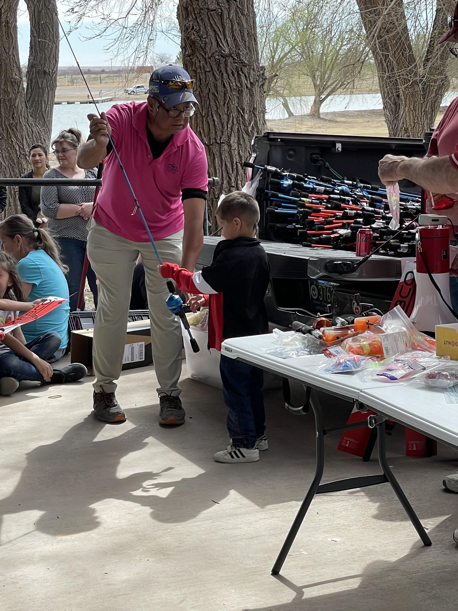 A lodge member helping a child use a fishing rod during an outdoor community activity
