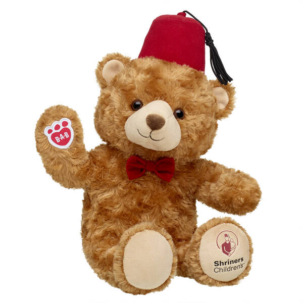Teddy bear wearing a red fez with Shriners Children’s logos on its paws